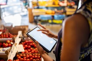 Woman looking at her electronic device while shopping for produce